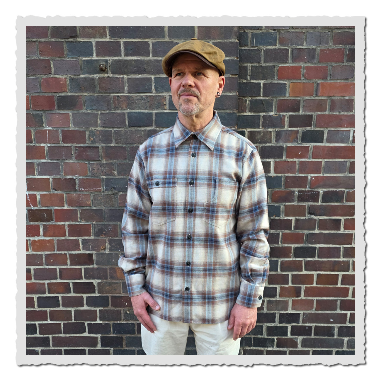 Mann vor Mauer trägt das Pike Brothers 1937 Roamer Shirt Stirling Brown – kariertes Flanellhemd